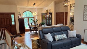 A spacious living area with a dark leather sofa, a light-colored ottoman, and a dining area with a wooden table and chairs.