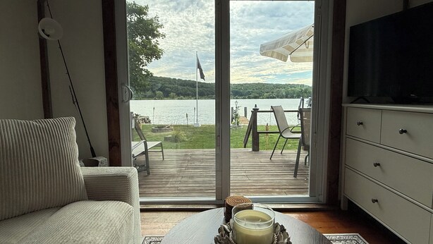 A living room with a sofa, a TV, and a view of a lake through a sliding glass door. - The little cottage on the ct river (Haddam)