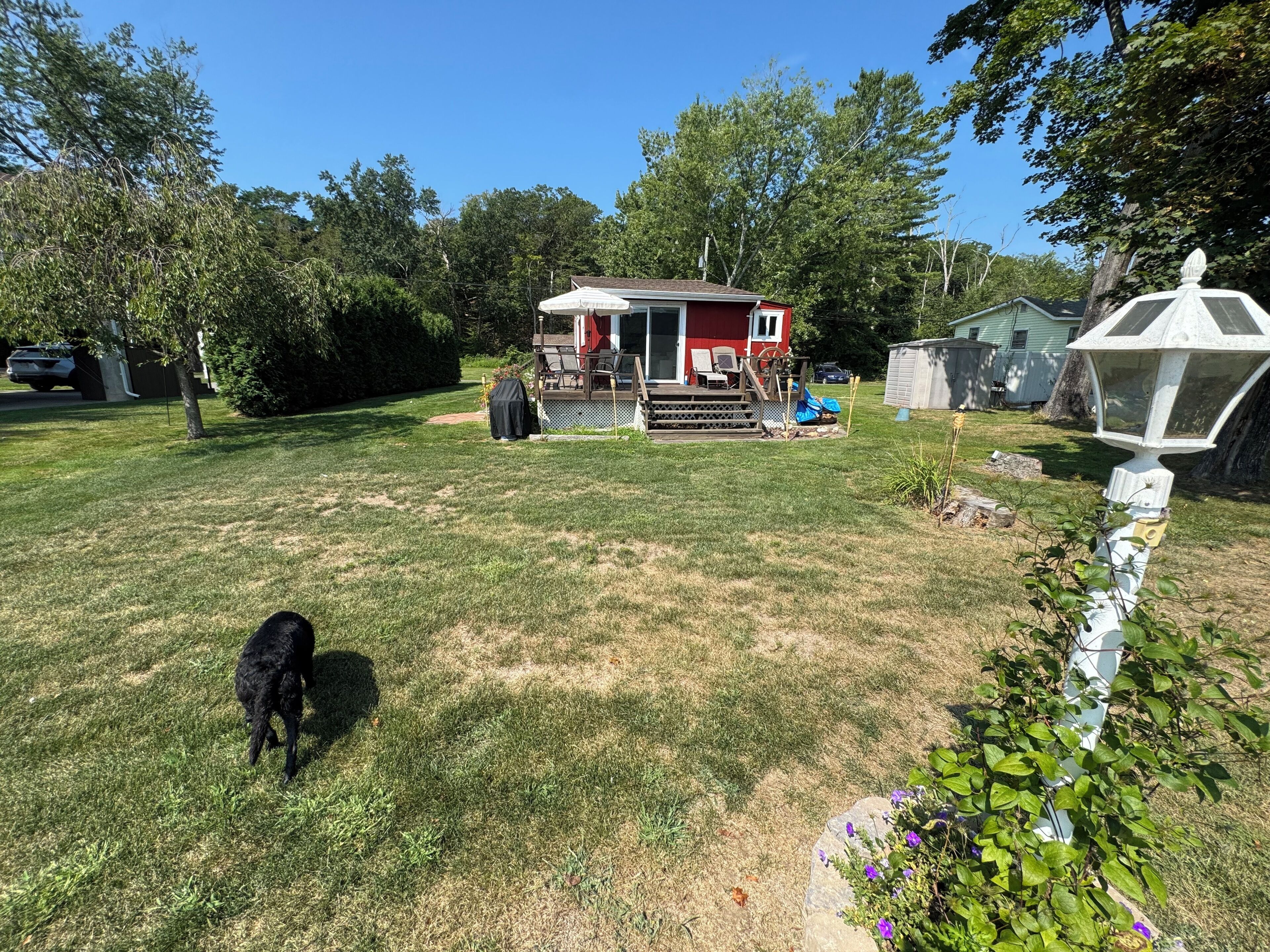A backyard with a red house, a covered patio, and a white lantern.