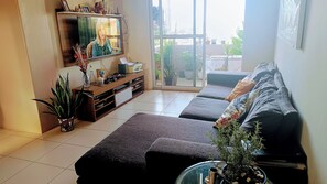 A living room with a sofa set, a TV, and a bookshelf. - Apartment with private bedroom and bathroom in Varjota, Fortaleza - Ceará. (Fortaleza)