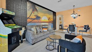 A modern living room with a 3D golf arcade, a sofa with cushions, a coffee table, and a dining area with chairs and a table. - Disney Family Resort: Home Theater, Pool & Free Parking/ Regal Palms Resort (Davenport)