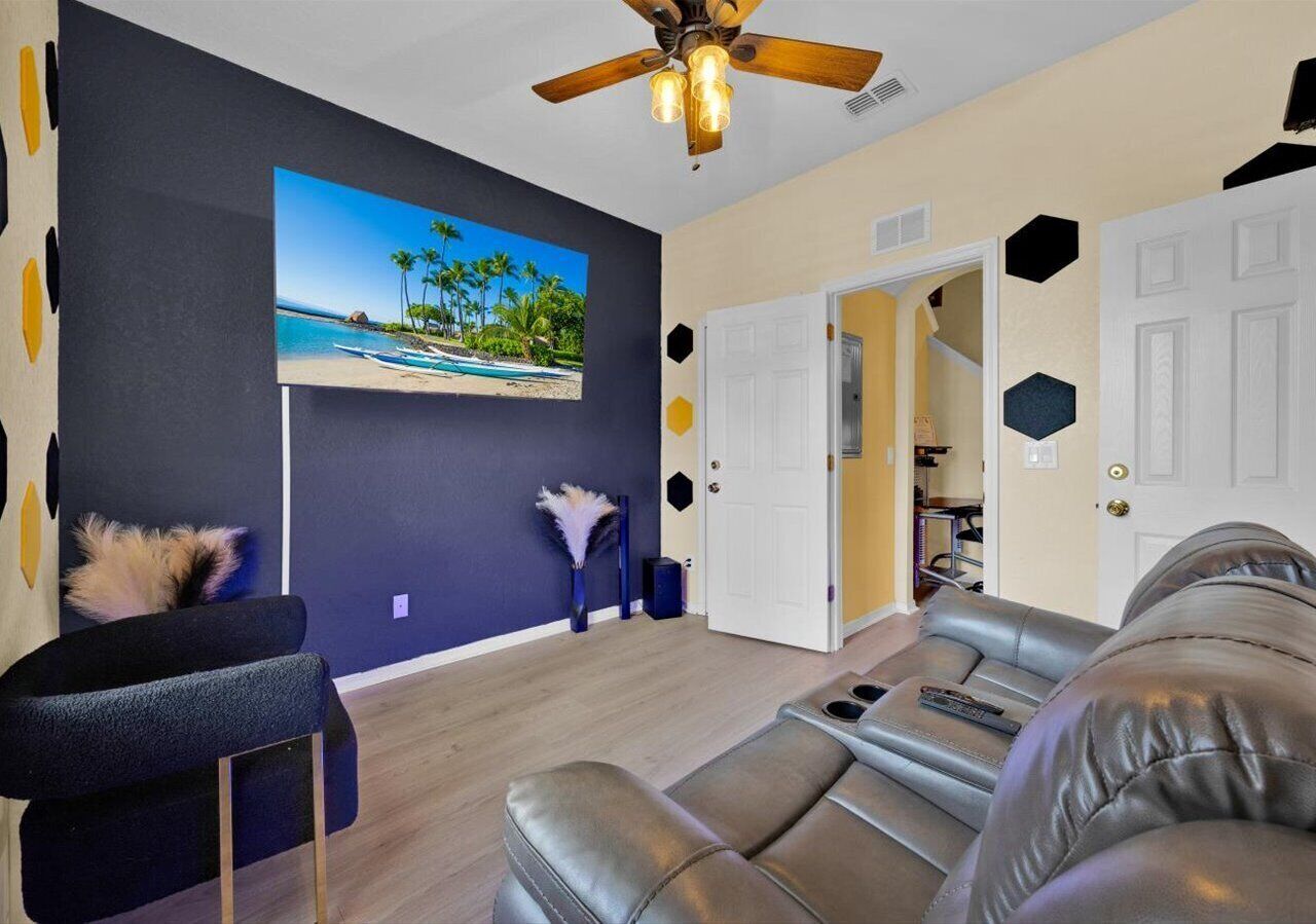 A living room with a dark blue wall, a ceiling fan, a sofa, a chair, and a door leading to another room.