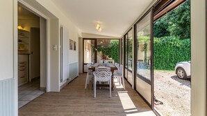 A dining area with a table set for four, a kitchen with cabinets and a countertop, and a view of a car and greenery outside. - LA PIERRE PONS - VOGLANS (VOGLANS)