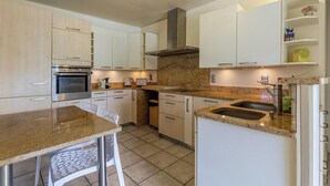 A modern kitchen with white cabinets, a granite countertop, a built-in oven, and a stainless steel sink. - LA PIERRE PONS - VOGLANS (VOGLANS)