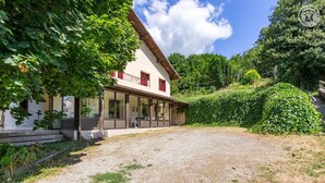 A two-story house with a covered patio, a gravel driveway, and a lush green garden. - LA PIERRE PONS - VOGLANS (VOGLANS)