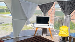 A tented room with a bed, a desk with a TV, and a chair. - Tihi Glamping Club (San Juan del Rio)