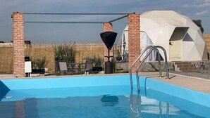 A swimming pool with a diving board, a covered seating area, and a dome-shaped structure in the background. - Tihi Glamping Club (San Juan del Rio)