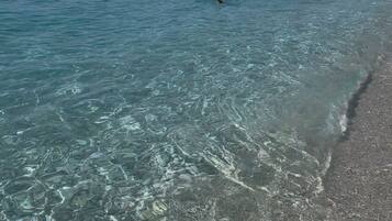 A clear beach with calm water, a distant boat, and a mountain in the background.