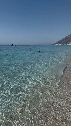 A clear beach with calm water, a distant boat, and a mountain in the background.