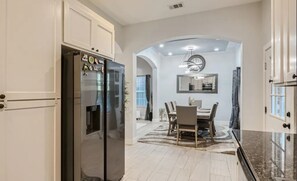Una cocina moderna con armarios blancos, un refrigerador de acero inoxidable y un comedor con mesa y sillas.
