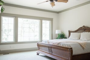 Ein Schlafzimmer mit großem Fenster, Deckenventilator und Holzbett.