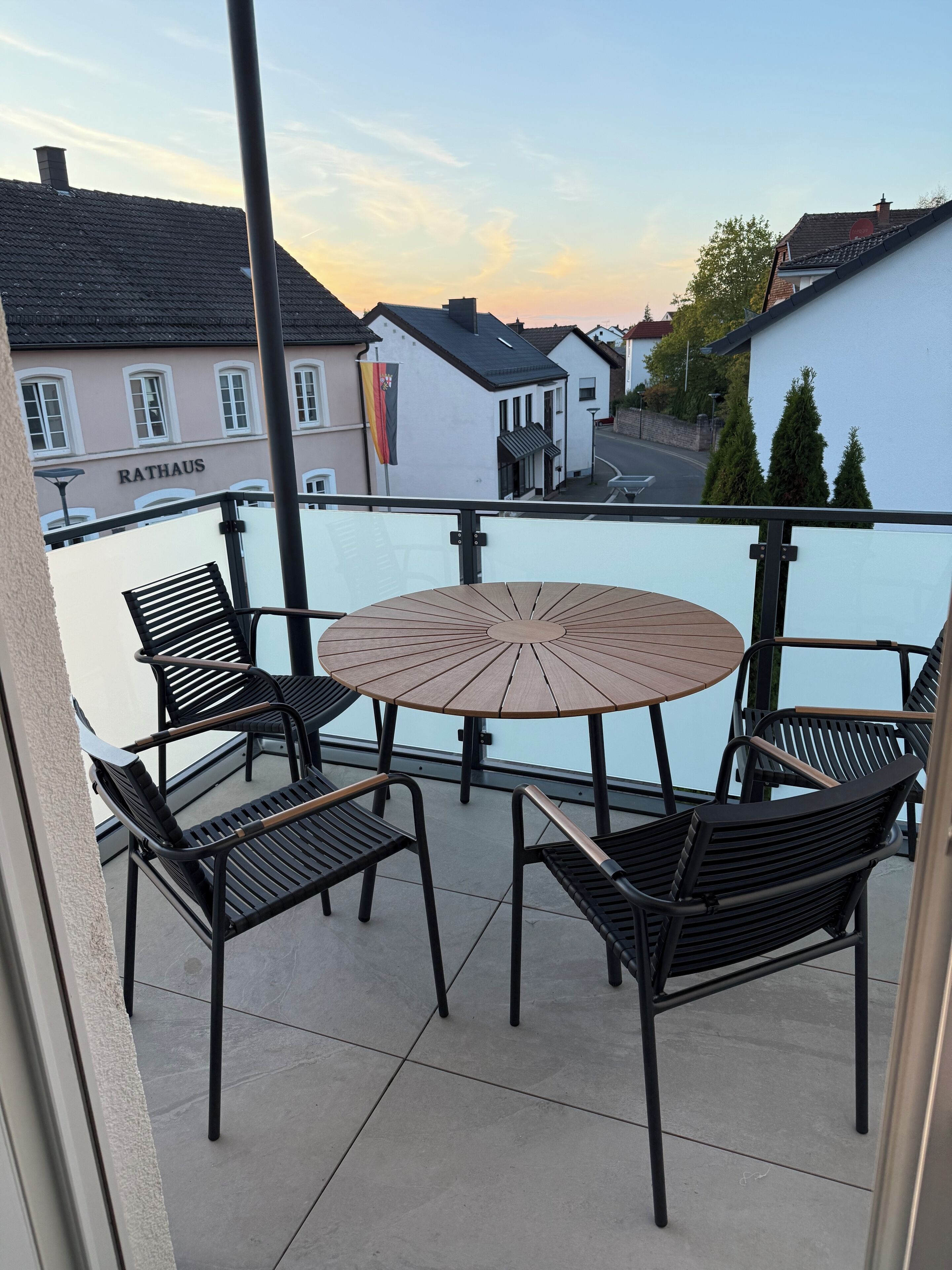 A balcony with a round table and four chairs, overlooking a body of water and buildings.