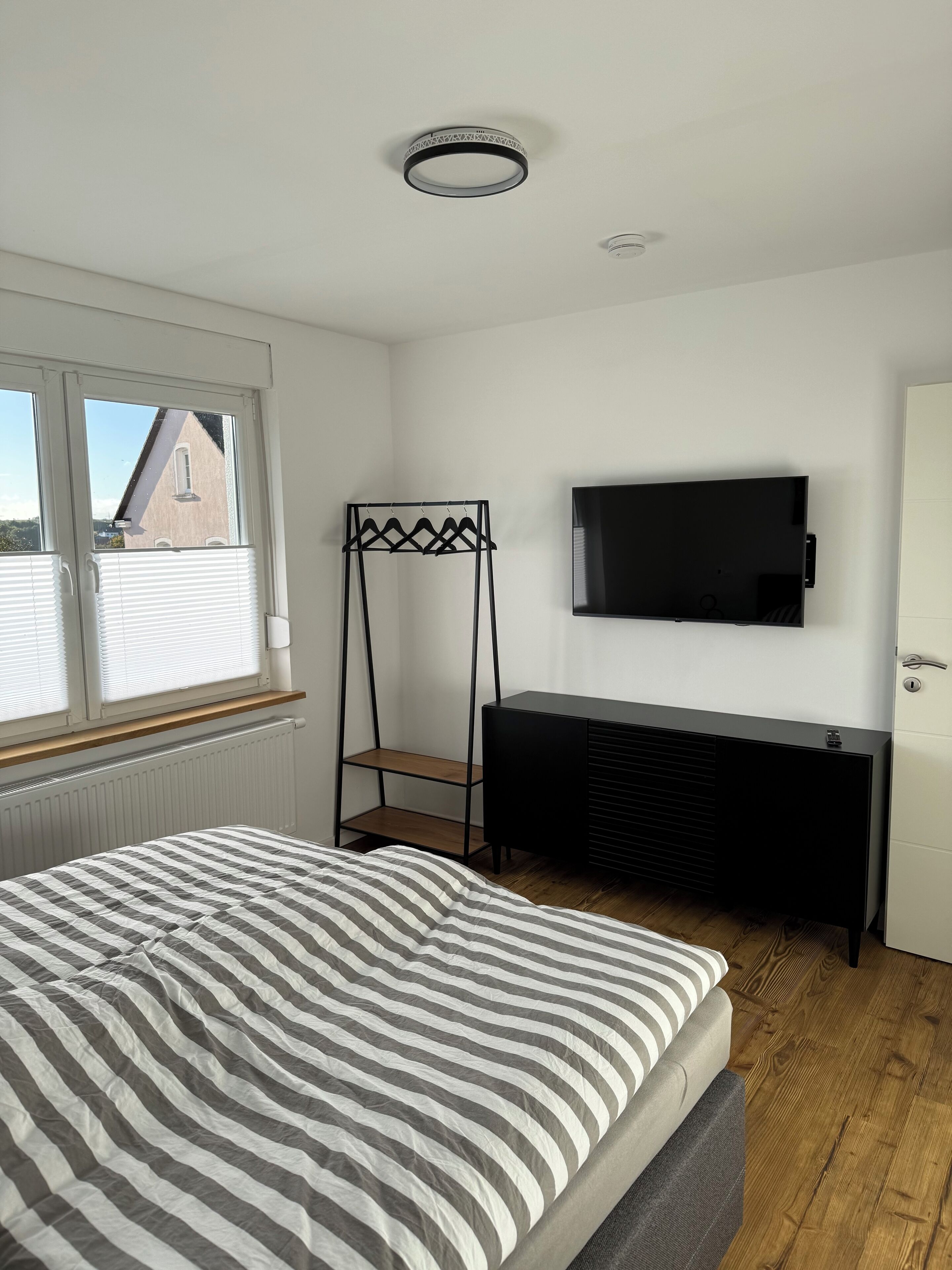 Een slaapkamer met een bed, een aan de muur bevestigde televisie, een radiator en een raam met zonwering.