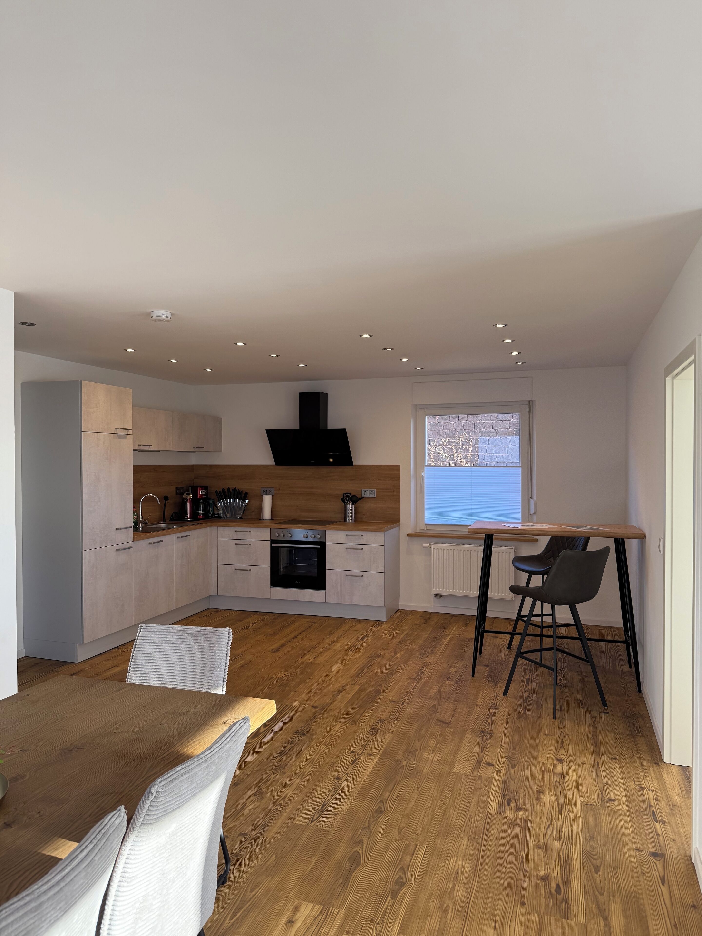 A modern kitchen with wooden cabinets, a built-in oven, and a window overlooking a brick wall.