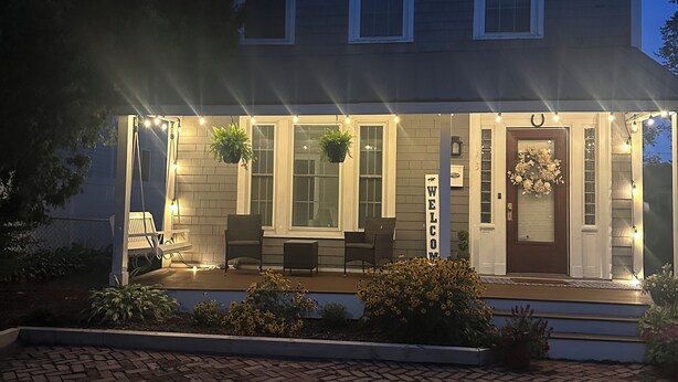 Une maison à deux étages avec un porche, un espace salon extérieur et une pancarte de bienvenue.
