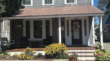 A two-story house with a porch, a front door, and a small garden with yellow flowers.
