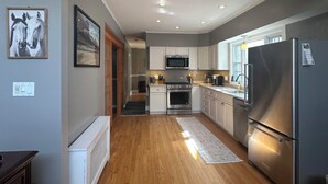 Une cuisine moderne avec un plancher en bois, des armoires blanches, des appareils électroménagers en acier inoxydable et des spots encastrés au plafond.