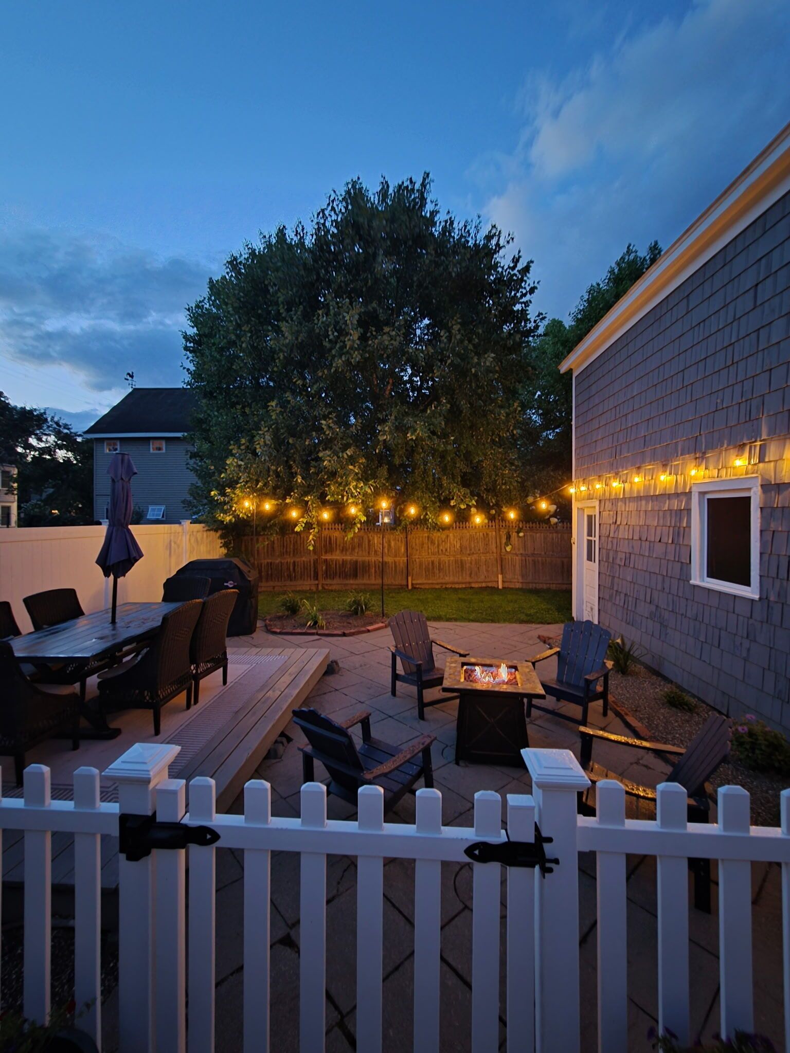 A backyard patio with outdoor furniture, a fire pit, and string lights.