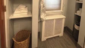 Un dressing ouvert avec des étagères, des paniers et une fenêtre avec des rideaux.