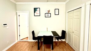 Een eetruimte met een witte tafel, vier zwarte stoelen, een witte deur en een witte muur met drie ingekaderde foto's.