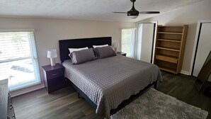 A bedroom with a bed, a nightstand, a lamp, a ceiling fan, a window with blinds, a wooden shelf, and a rug. - Cozy retreat in Athens - convenient location, walk to Five Points, close to UGA. (Athens)