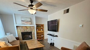 A living room with a fireplace, a ceiling fan, a TV mounted on the wall, and a wooden coffee table. - Cozy retreat in Athens - convenient location, walk to Five Points, close to UGA. (Athens)