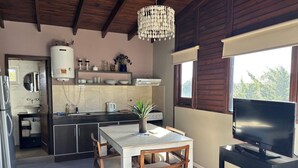 Een moderne keuken met een inbouwoven, een eettafel met stoelen, een televisie op een standaard en een groot raam.