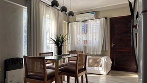 Een eethoek met een glazen tafel, houten stoelen en een potplant.