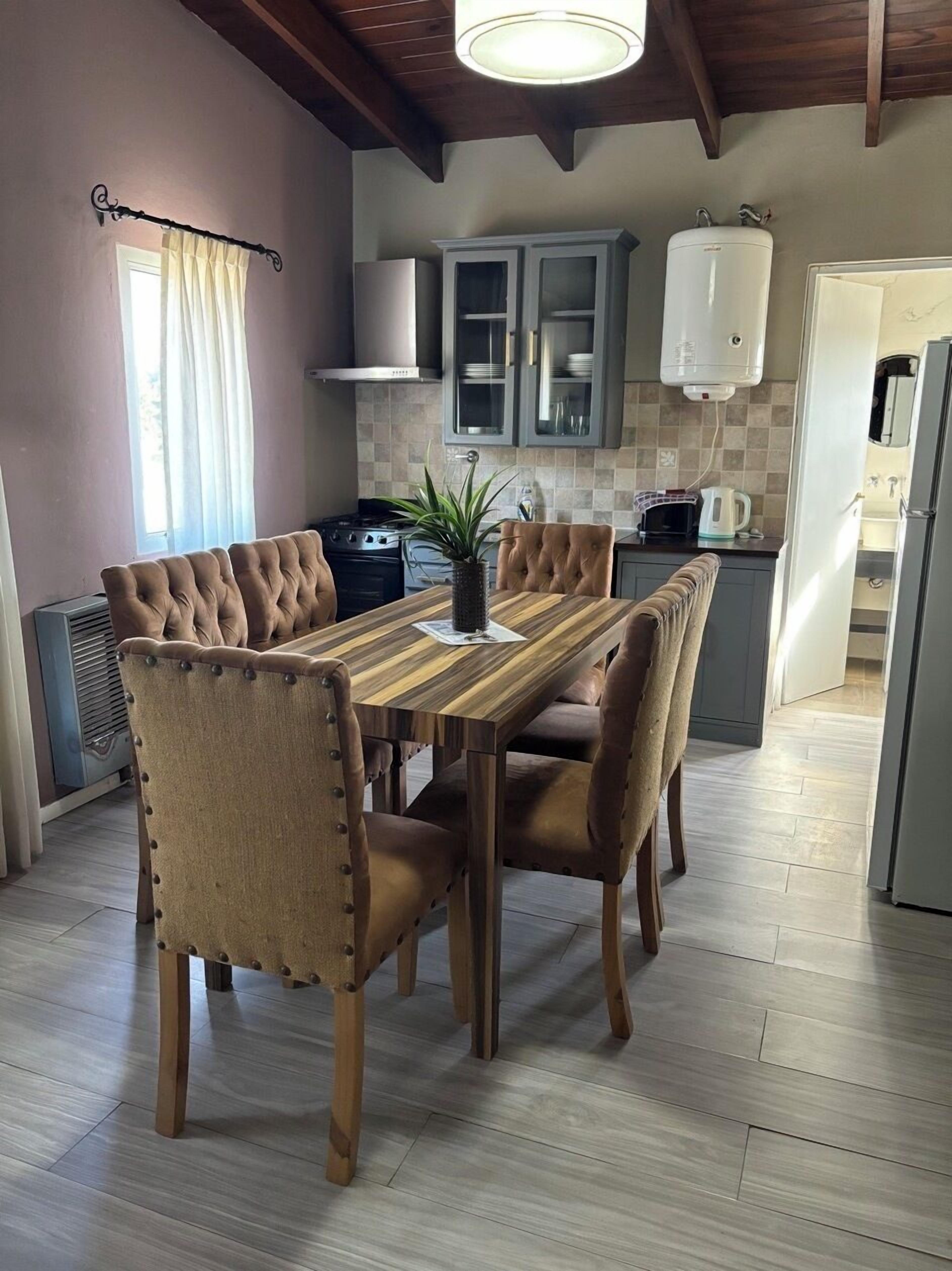 Un comedor con mesa de madera y sillas tapizadas, una cocina con electrodomésticos modernos y un techo con vigas a la vista.