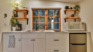 Una cocina con armarios blancos, un lavamanos doble, un microondas y un refrigerador.