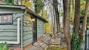 Una cabaña rústica con un sendero de piedra que conduce a la puerta, rodeada de árboles y una cerca de madera.