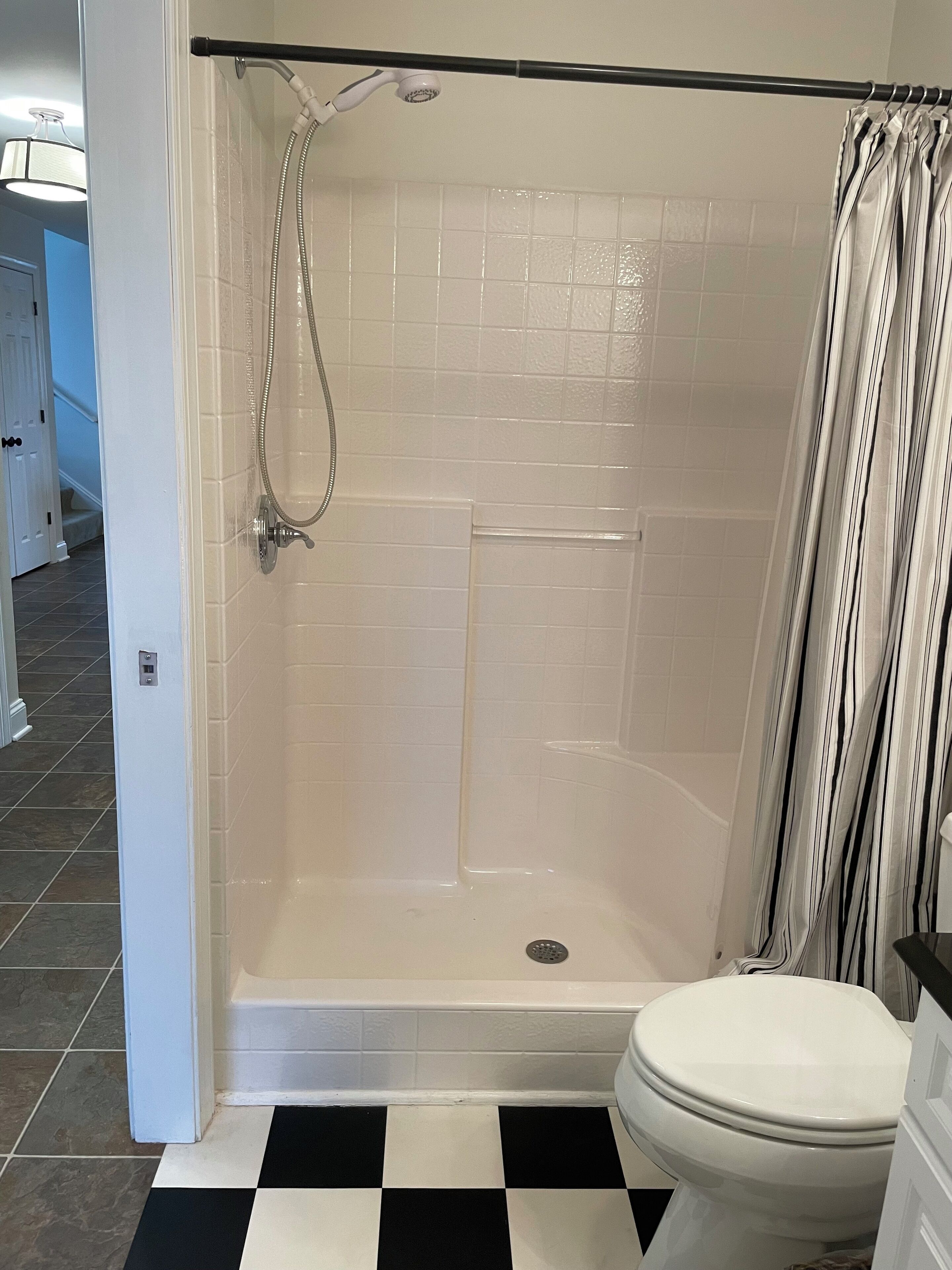 Un baño con ducha, inodoro y suelo de baldosas a cuadros.