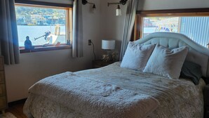 Ein Schlafzimmer mit einem großen Bett, Holzbalkendecke, einem Fenster mit Blick auf Boote und Gebäude sowie einem Nachttisch mit Lampe.
