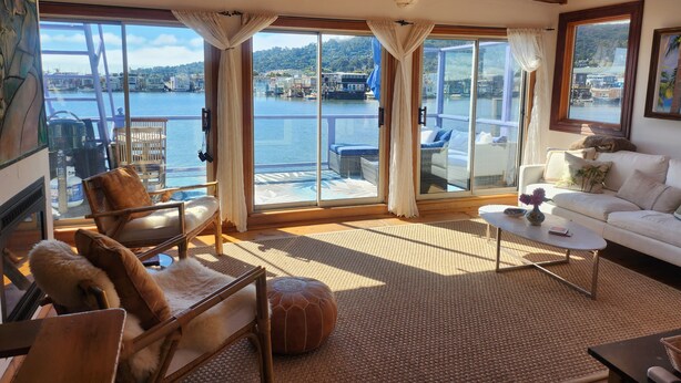 Ein geräumiger Wohnbereich mit großem Fenster mit Blick auf ein Gewässer, Deckenventilator und ein weißes Sofa.