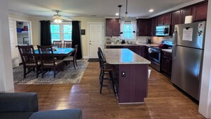 A modern kitchen with a central island, dark wooden cabinets, stainless steel appliances, and a dining area with a table and chairs.
