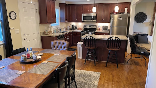 A modern kitchen with dark wooden cabinets, stainless steel appliances, and a dining area with a wooden table and chairs.