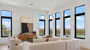 A modern living room with a large sectional sofa, a wooden cabinet, and large windows offering a view of the outdoors.