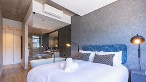 Ein modernes Hotelzimmer mit einem großen Bett, einem Badezimmer mit einer Badewanne und einem Kleiderschrank.