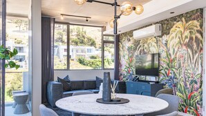 Ein modernes Wohnzimmer mit einem runden Tisch, grauen Sofas, einem großen Fernseher und einem tropischen Wandbild.
