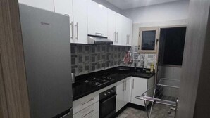A compact kitchen with white cabinets, a stainless steel refrigerator, a gas stove, and a tiled backsplash. - Chambre calme (Amizmiz)