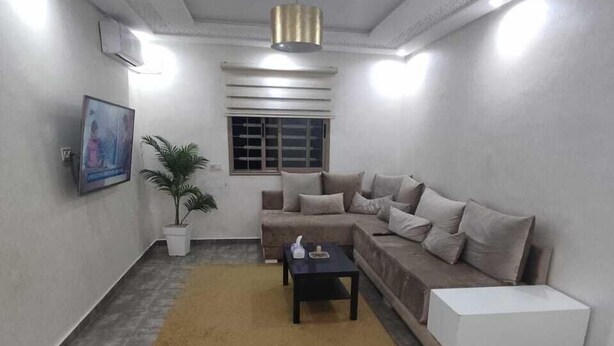 A modern living room with a grey sofa, a coffee table, a small white side table, a potted plant, and a framed picture on the wall. - Chambre calme (Amizmiz)