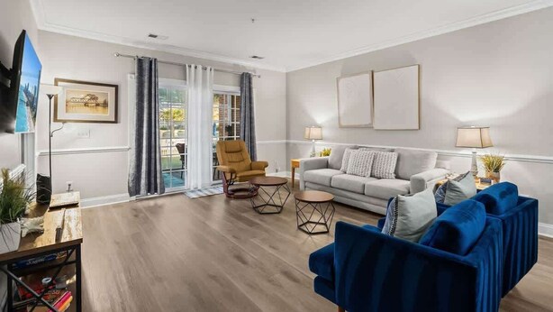 Un salon moderne comprenant un canapé, un fauteuil et une table basse, un téléviseur et un balcon avec des rideaux.