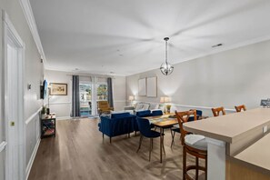 A modern dining area with a long table, blue upholstered chairs, and a chandelier.