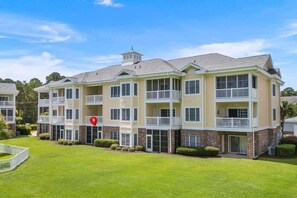 A multi-story residential building with balconies, a central tower, and a well-maintained lawn.