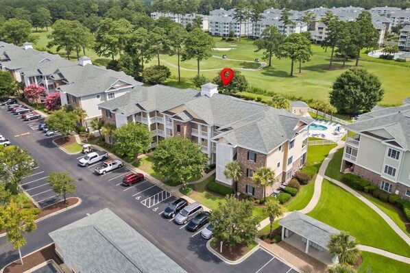 A residential area with multiple two-story houses, a parking lot, and a golf course in the background.