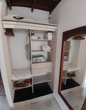 A walk-in closet with multiple shelves, drawers, and hanging space, featuring a mirror and a wooden ceiling.