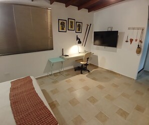 A bedroom with a bed, a desk, a chair, a TV, and a window with blinds. - Envigado, studio apartment, quiet, safe. (Envigado)