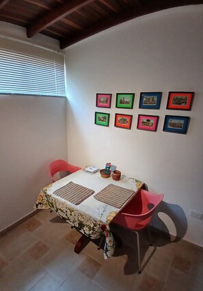 A dining area with a table set for two, a red chair, and a wall adorned with framed pictures.