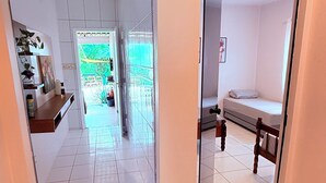 Un couloir avec un mur recouvert de miroirs, qui mène à une pièce contenant un lit et un banc.