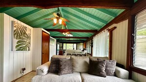 Un espacio de sala acogedor con un sofá, cojines estampados, un ventilador de techo y un ventanal grande.